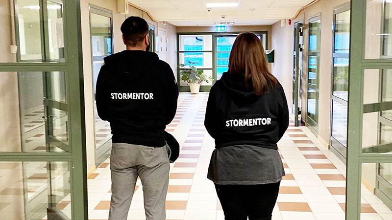Stormentor Två personer som står med ryggen mot kameran och på deras ryggar står det stormentor.
